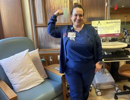 White woman in scrubs flexing her arm to signify strength. 