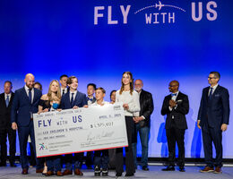 Hospital leadership, staff, and patient stand on stage holding large check with total number of funds raised at charity event