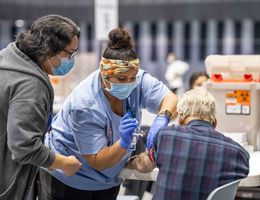 Nurse in blue scrubs giving a vaccine to a senior citizen as someone else looks on