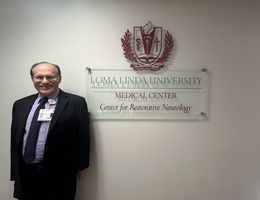 man standing in suit smiling in front of sign that reads loma linda university medical center center for restorative neurology 