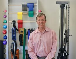 Mark Bussell, DPT, sits in front of physical therapy equipment