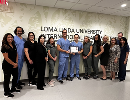 Care team members of the Structural and Valvular Heart Disease program at Loma Linda University Medical Center gather around and pose with their certification from the American College of Cardiology for transcatheter valve care in adult cardiac patients.