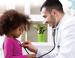 male doctor puts stethoscope on little girl's chest