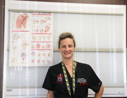 Dr. Rajfer stands next to a poster of the shoulders anatomy as she smiles at the camera