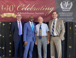 Four men stand in front of banner that reads "Celebrating 40 years of Rehabilitation Services"