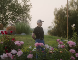 Young hispanic stands in garden with arms relaxed behind his back. 