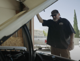 Man stands looking in hood of vintage car.