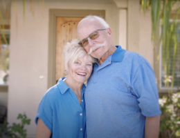 Elderly caucasian couple stands smiling side by side both wearing light blue. 