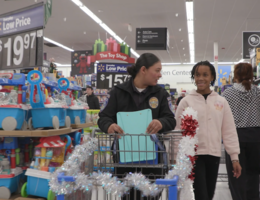 A female officer walks alongside a pediatric RICA patient in Walmart with a Christmas decorated shopping cart filled with toys.