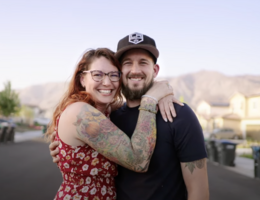 Justin Telesio wears a black shirt which his wife, Amie, wears a red dress and they stand outside and hug