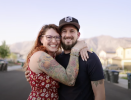 Justin Telesio wears a black shirt which his wife, Amie, wears a red dress and they stand outside and hug