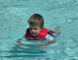 Young boy swims in pool with US Coast-guard approved life vest