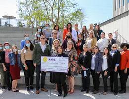 group of child life specialists and hospital administrators stand with giant check in outdoor amphitheater smiling at camera