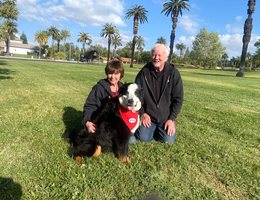 Husand and wife sit in a field with their therapy dog named Emma