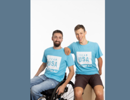 two Caucasion males, one in a wheelchair in blue t-shirts