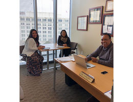 Two women and one man sit in office with large window