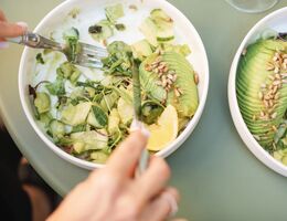 Overhead view of a woman eating a green salad with avocado, cucumber and toasted sunflower seeds 