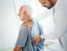 physician checks elderly mans back for pain