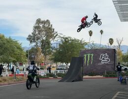 Three motocross riders doing tricks off ramp in front of Hospital for patients