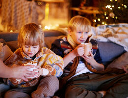 Two young boys sitting on a couch drinking hot chocolate 