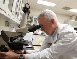 White male looking into a microscope inside a research lab