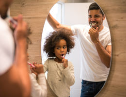 Father and daughter brush teeth in a mirror