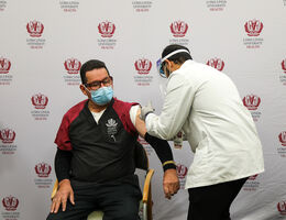 male hospital worker receives COVID-19 vaccine from male pharmacy student