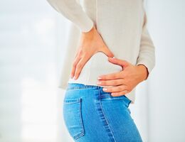 A woman in a white sweater and jeans holds her hip with pain