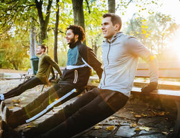 young men are leaning on a bench and stretching in a wooded forest 