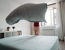  A woman makes her bed, the sheet billowing in the air above the mattress