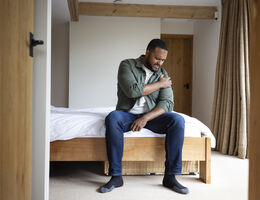 A mid adult man sitting on the edge of his bed in the bedroom at home