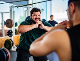 Mid adult man doing squats with personal trainer at gym