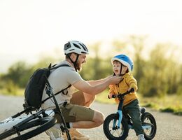 A father kneeling down to strap on a helmet for a young boy