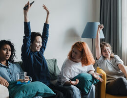 Four friends gather in a comfortable living room, animatedly watching sports. They express excitement, showing various emotions as they cheer for their favorite team.