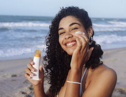 Young woman applying sunscreen on her face at the beach