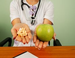 Woman displays a handful of pills versus a green apple.