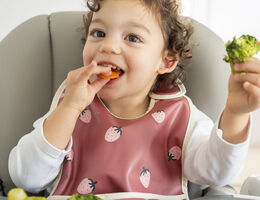 Young child sitting in highchair eating carrots and broccoli