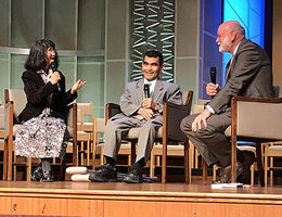 Two men and a woman sit in chairs on stage holding microphones