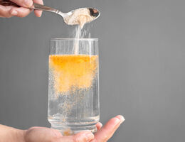 Pouring orange powder, alluding to electrolyte supplements, into clear water glass