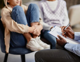Close up of African-American psychologist taking notes on clipboard in therapy session for children