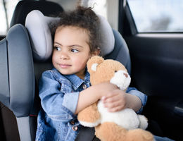 little girl holding teddy bear while sitting in car