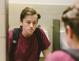 Depressed teen looks at himself in bathroom mirror stock photo