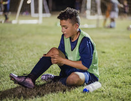 Young soccer player sitting on the grass nursing an injury.