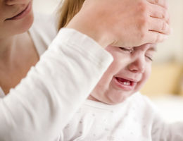 Mother holding her baby, checking his temperature with her hand.