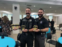 Two officers stand side by side holder trophies, smiling