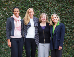Four women smile in front of foliage