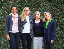 Four women smile in front of foliage