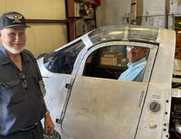 Joe Yancey shows Dr. Akhtari his hangar as Dr. Akhtari sits in a world war II plane cockpit