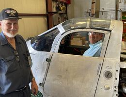 Joe Yancey shows Dr. Akhtari his hangar as Dr. Akhtari sits in a world war II plane cockpit