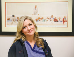 female nurse poses for photo in front of picture of Dr. Bailey and children he helped